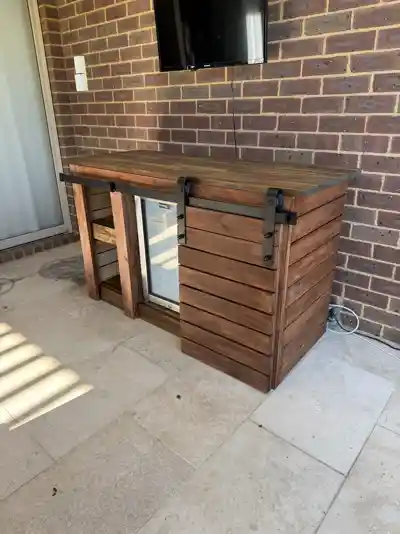 Finished timber outdoor bar against a brick wall, sliding barn door closed over the fridge bay.